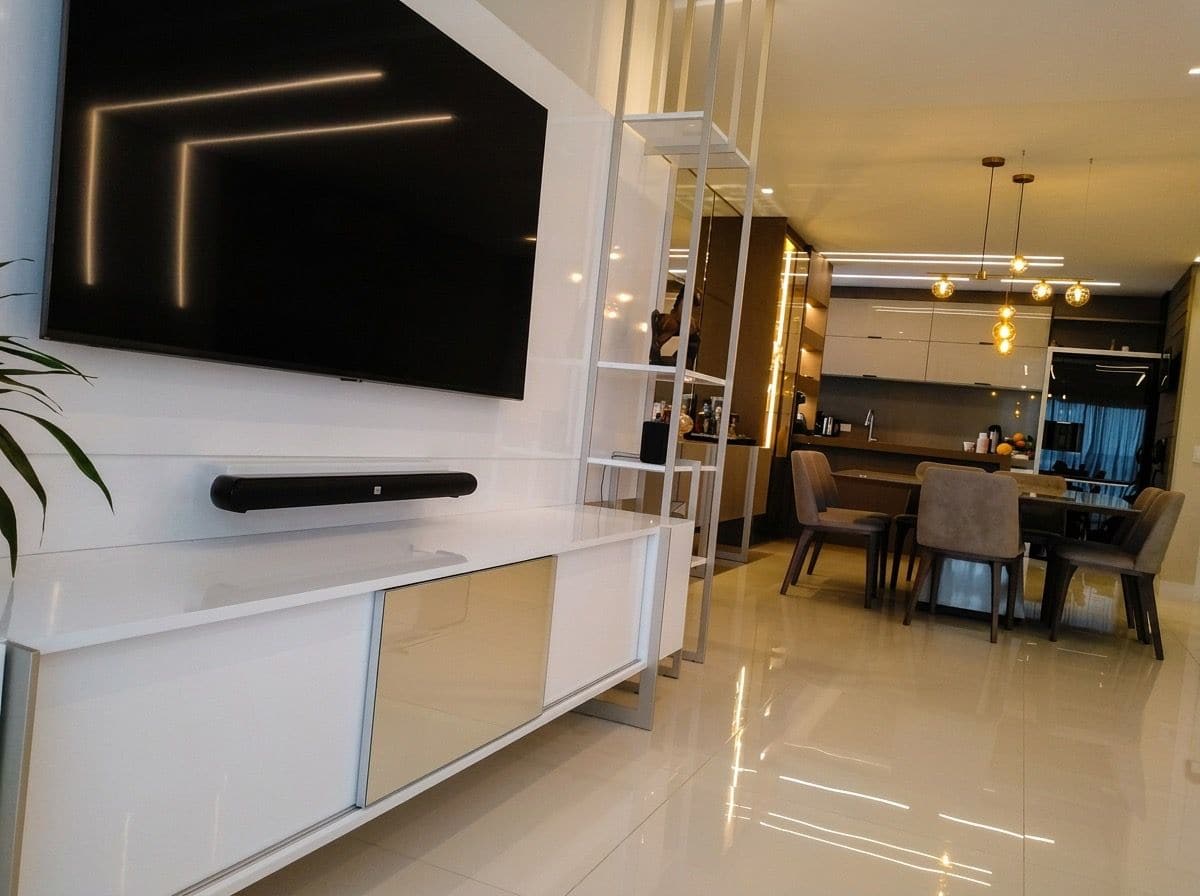 Painel de TV em branco alto brilho com rack suspenso e porta em vidro bronze, estante metálica vazada separando a sala da cozinha e da mesa de jantar ao fundo